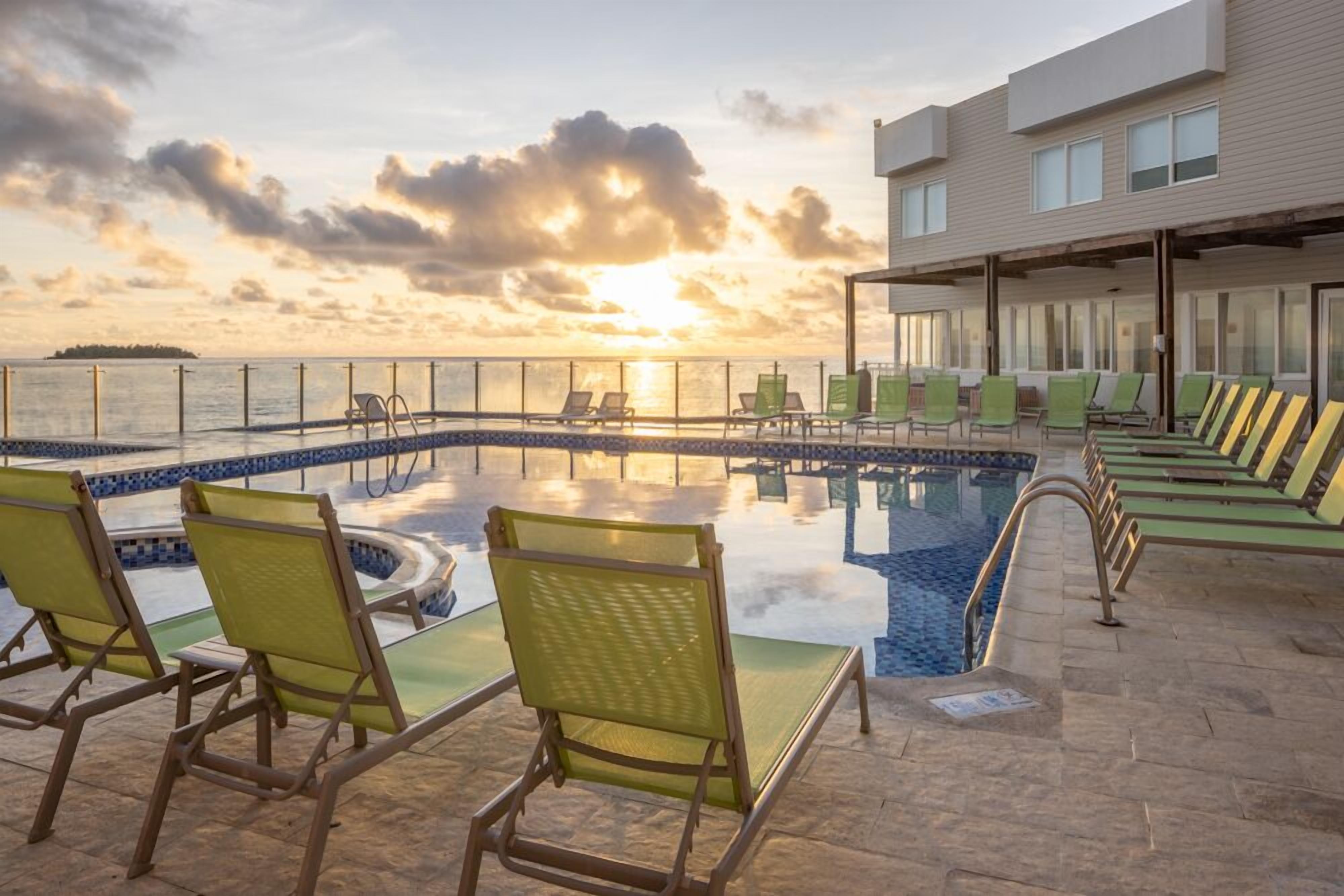 A poolside area with lounge chairs and a view of the sunset over the water.