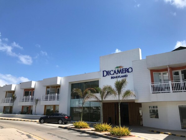 Un hotel llamado Decamero Maryland con fachada blanca moderna, varios balcones y un coche estacionado al frente.