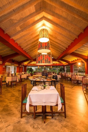 Un comedor con una mesa central dispuesta para una comida, rodeada de sillas, bajo un techo de madera con una lámpara decorativa.