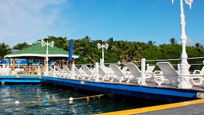 A pier with lounge chairs and a building with a green roof. - Decameron Marazul - All Inclusive (San Andrés)