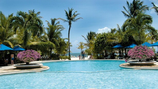 A pool area with palm trees, lounge chairs, and a view of the ocean. - Decameron Marazul - All Inclusive (San Andrés)
