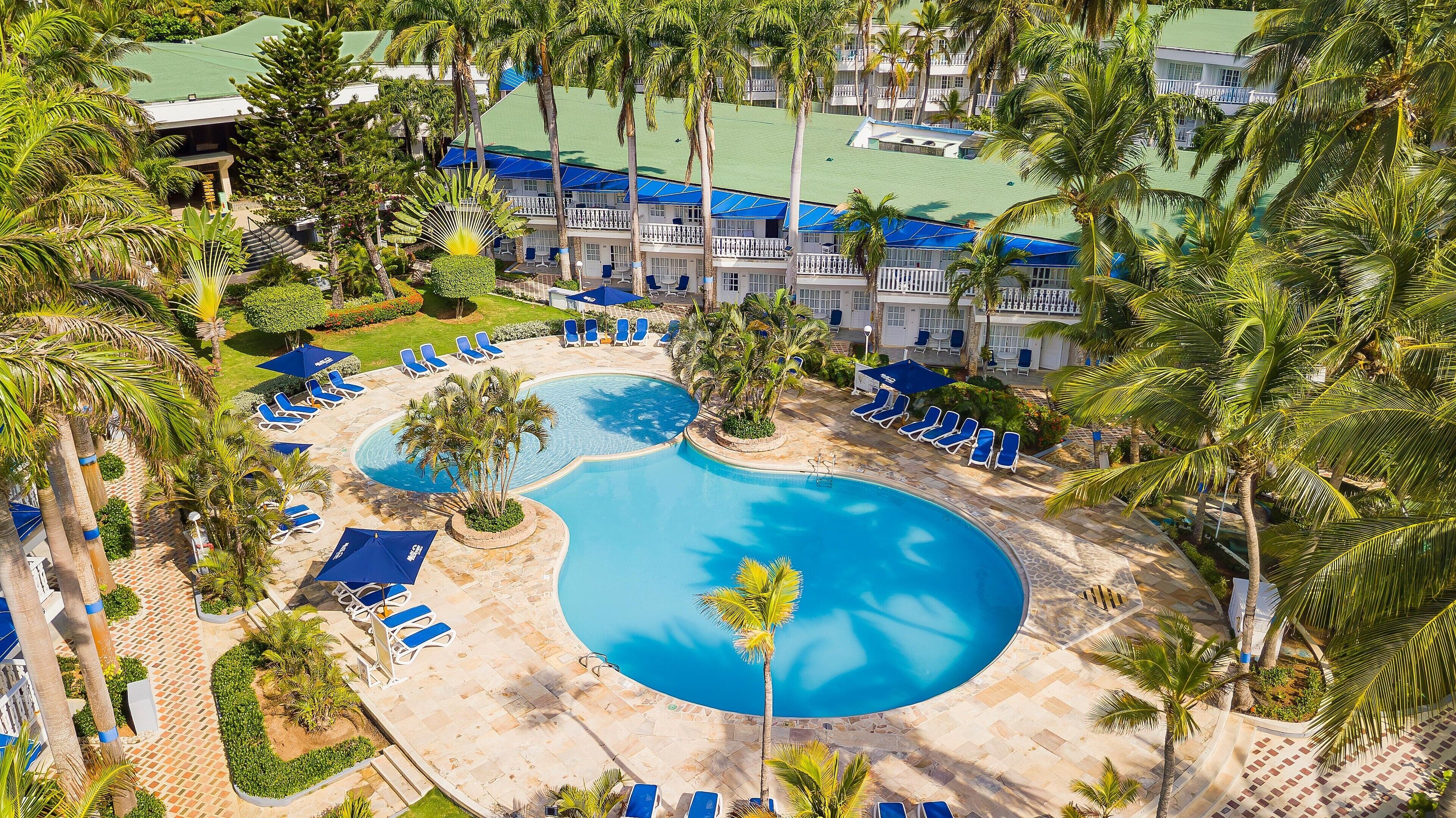Ein Resort mit großem Swimmingpool, umgeben von Palmen und Liegestühlen.