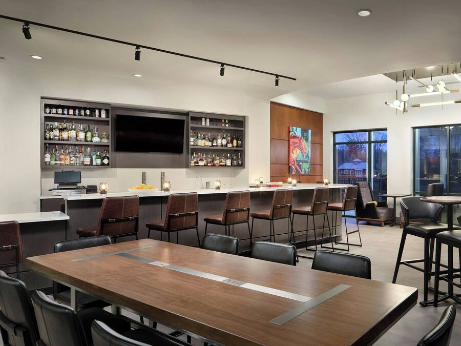 A modern bar area with a long counter, multiple seating options, and a large TV screen.