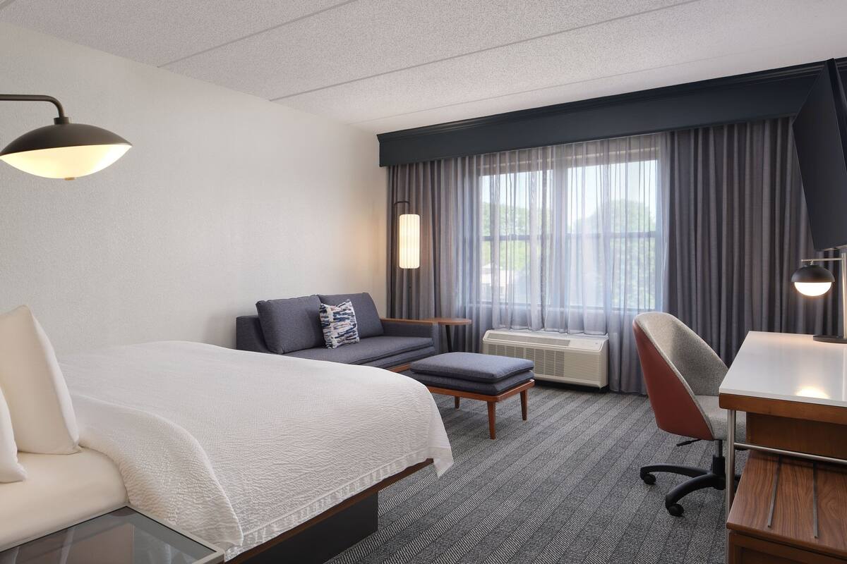 Ein Hotelzimmer mit einem großen Bett, einem Schreibtisch, einem Sessel, einer Couch und einem Fenster mit Vorhängen.