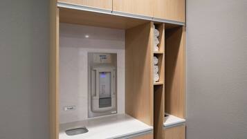 A modern bathroom with a built-in water dispenser, a trash bin, and neatly folded towels on shelves.