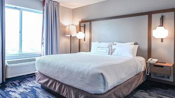 A hotel room with a large bed, a bedside table with a lamp, a phone, and a window with curtains.