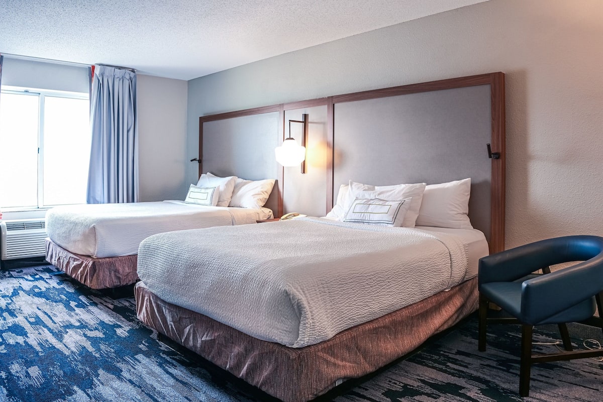 Ein Hotelzimmer mit zwei Betten, einem blauen Teppich mit Muster und einer modernen Lampe.