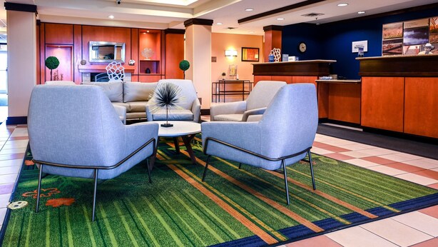 A lobby with two armchairs, a coffee table, a reception desk, and a fireplace. - Fairfield Inn & Suites by Marriott Indianapolis Noblesville (Noblesville)