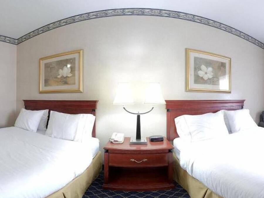 A hotel room with two single beds, a nightstand with a lamp, a phone, and a small table.