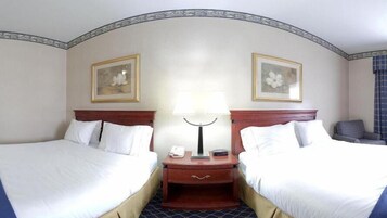 Habitación de hotel con dos camas individuales, una mesita de noche con lámpara, teléfono y una pequeña mesa.