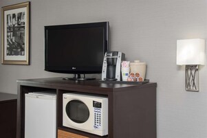 Una kitchenette compacta con microondas, cafetera y televisor de pantalla plana sobre un mueble de madera oscura.
