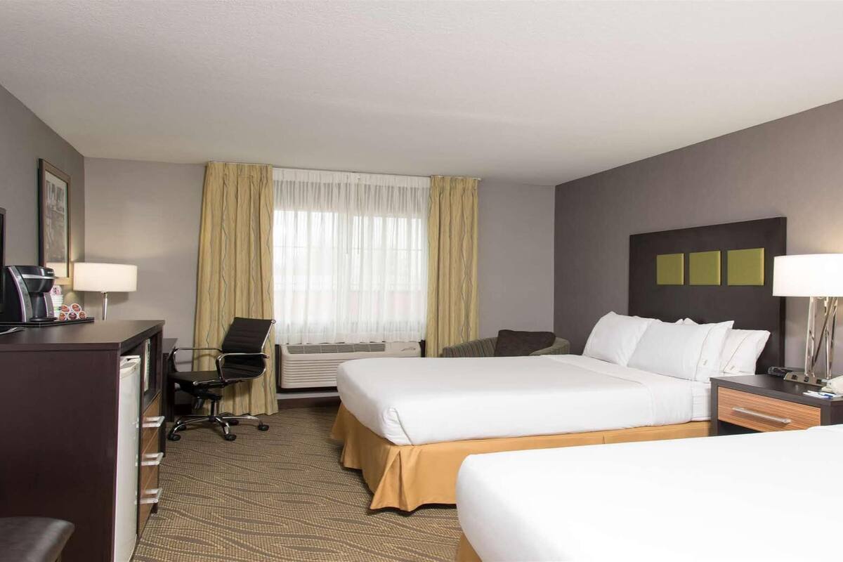 A hotel room with two beds, a desk with a computer, a chair, a desk lamp, and a telephone.