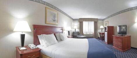 A hotel room with a large bed, bedside tables, a desk, a chair, a television, and a framed picture on the wall.