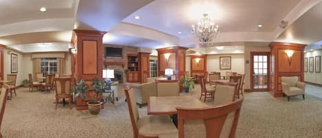 A spacious lobby with a high ceiling, chandeliers, and a fireplace. There are multiple seating areas with tables and chairs.