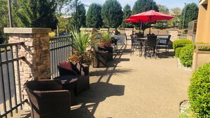 An outdoor patio area with wicker furniture, a red umbrella, and neatly trimmed bushes. - Hampton Inn Lewisburg (Lewisburg)