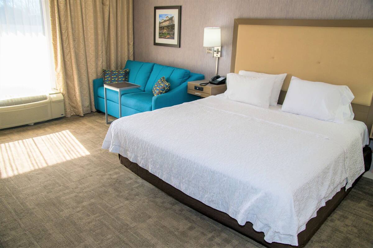 Habitación de hotel con una cama grande, un sofá azul, una mesita y una lámpara.