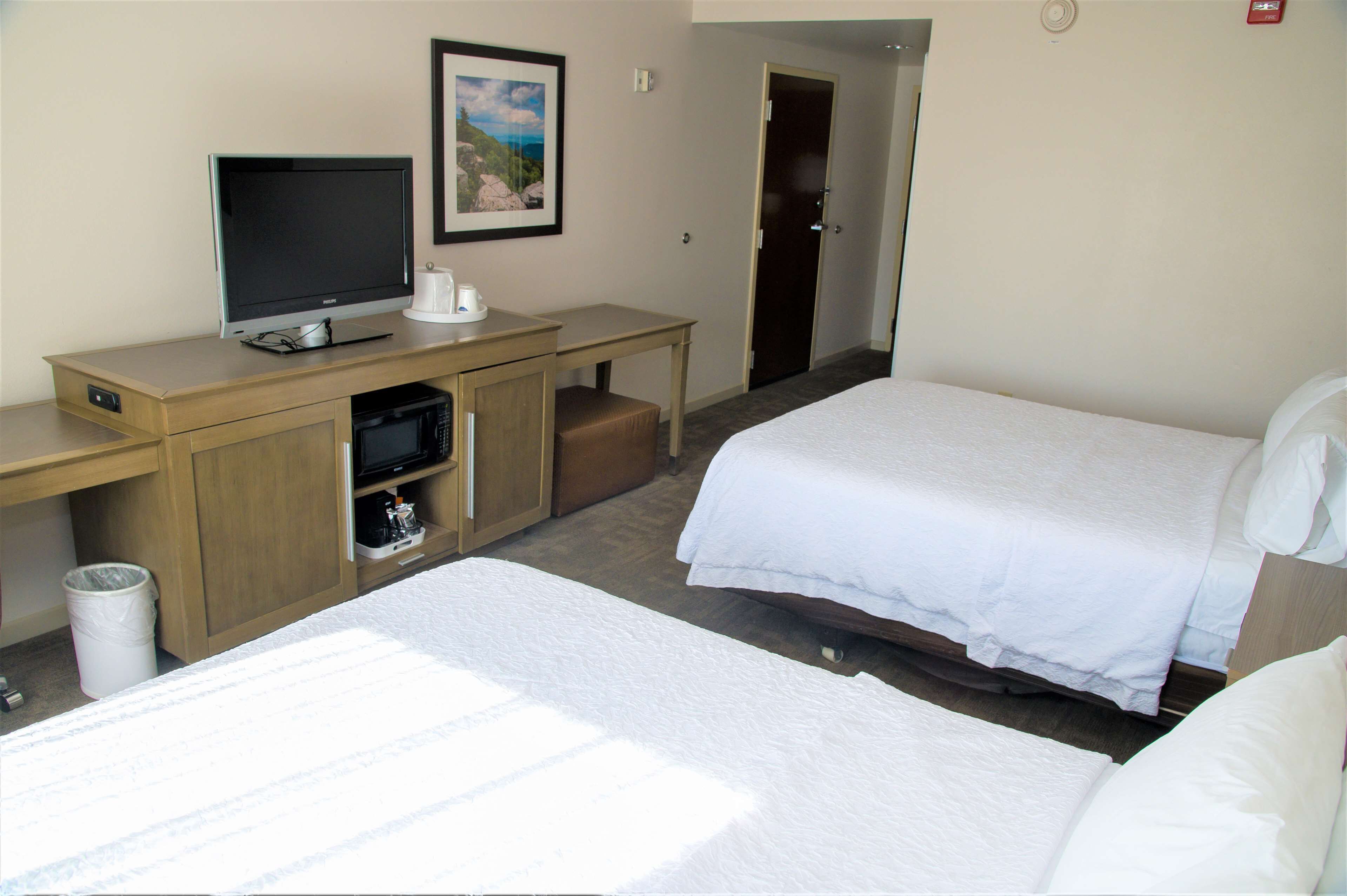 Une chambre d’hôtel avec deux lits, un bureau avec une télévision et une petite poubelle.
