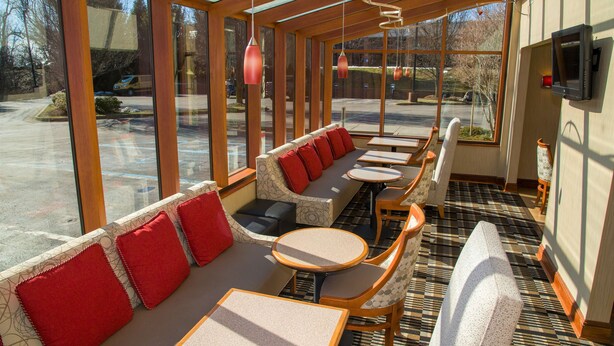 A sunlit indoor seating area with a sofa, chairs, and tables, large windows, and a television on the wall. - Hampton Inn Lewisburg (Lewisburg)