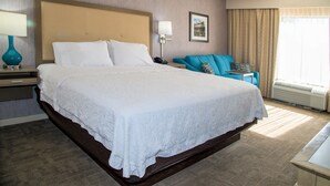 A hotel room with a large bed, a bedside table with a lamp, a chair, a picture on the wall, and a window with curtains. - Hampton Inn Lewisburg (Lewisburg)