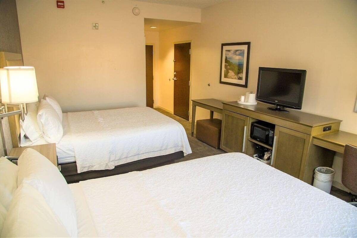 Habitación de hotel con dos camas, un escritorio con televisor y microondas.