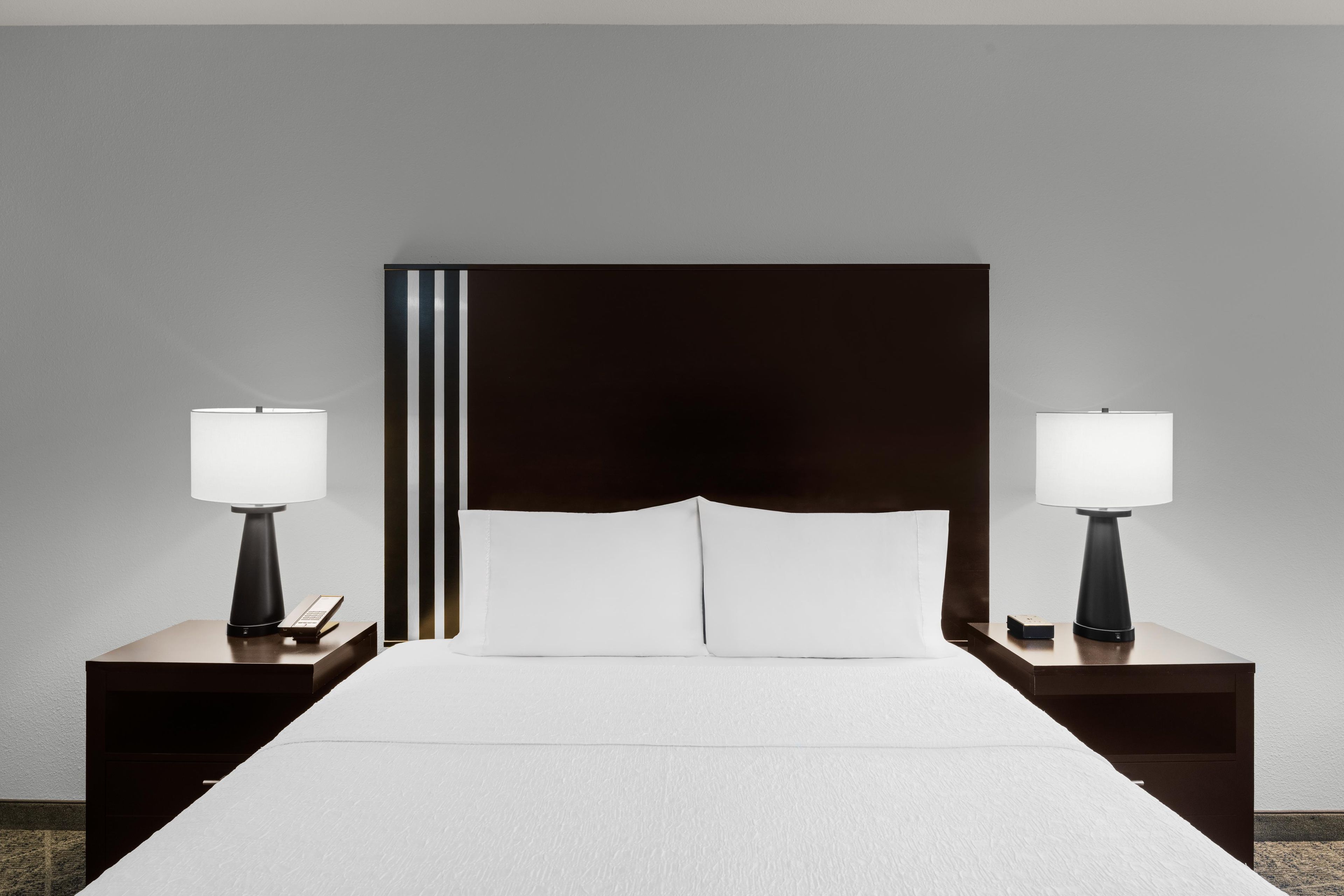 A hotel room with a large bed, two bedside tables with lamps, and a dark headboard.