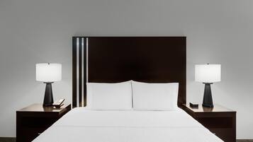 A hotel room with a large bed, two bedside tables with lamps, and a dark headboard.