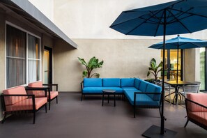 A modern indoor patio with a blue sofa, red chairs, and a large umbrella. - Hampton Inn & Suites Mountain View (Mountain View)