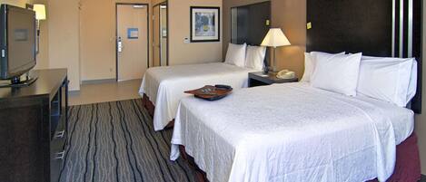 A hotel room with two beds, a TV, a desk, and a lamp.