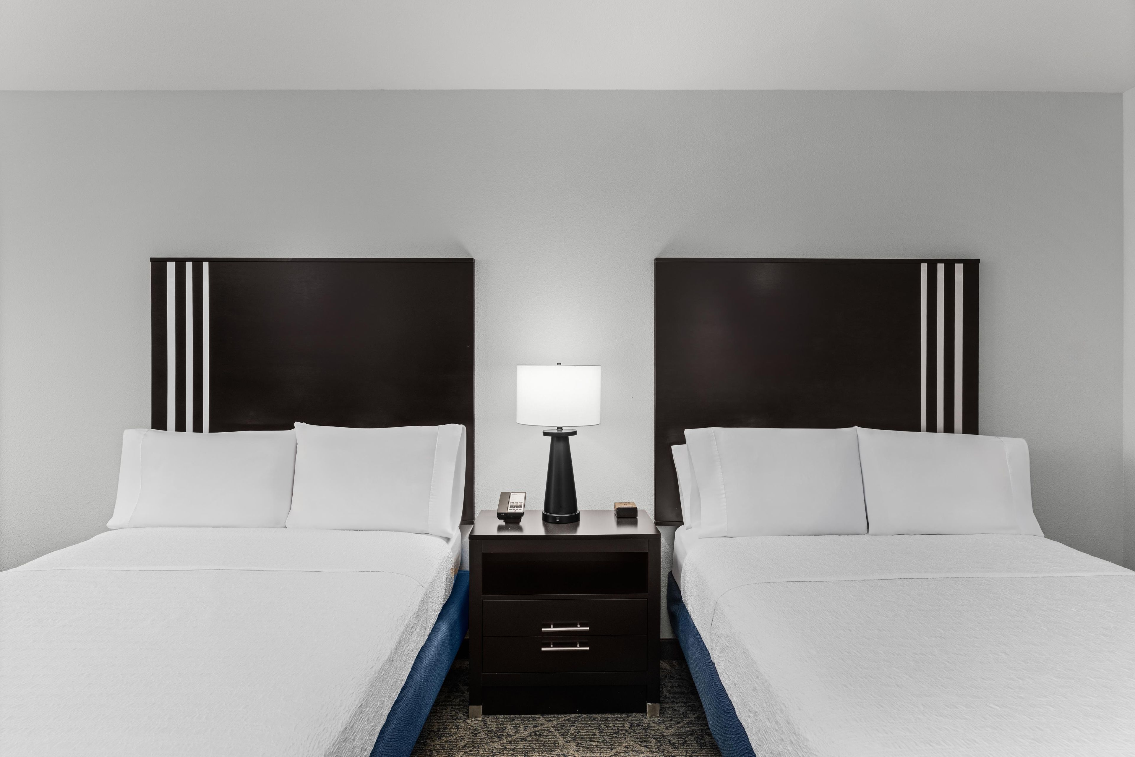 Une chambre d’hôtel avec deux lits, une table de chevet avec une lampe et une commode.