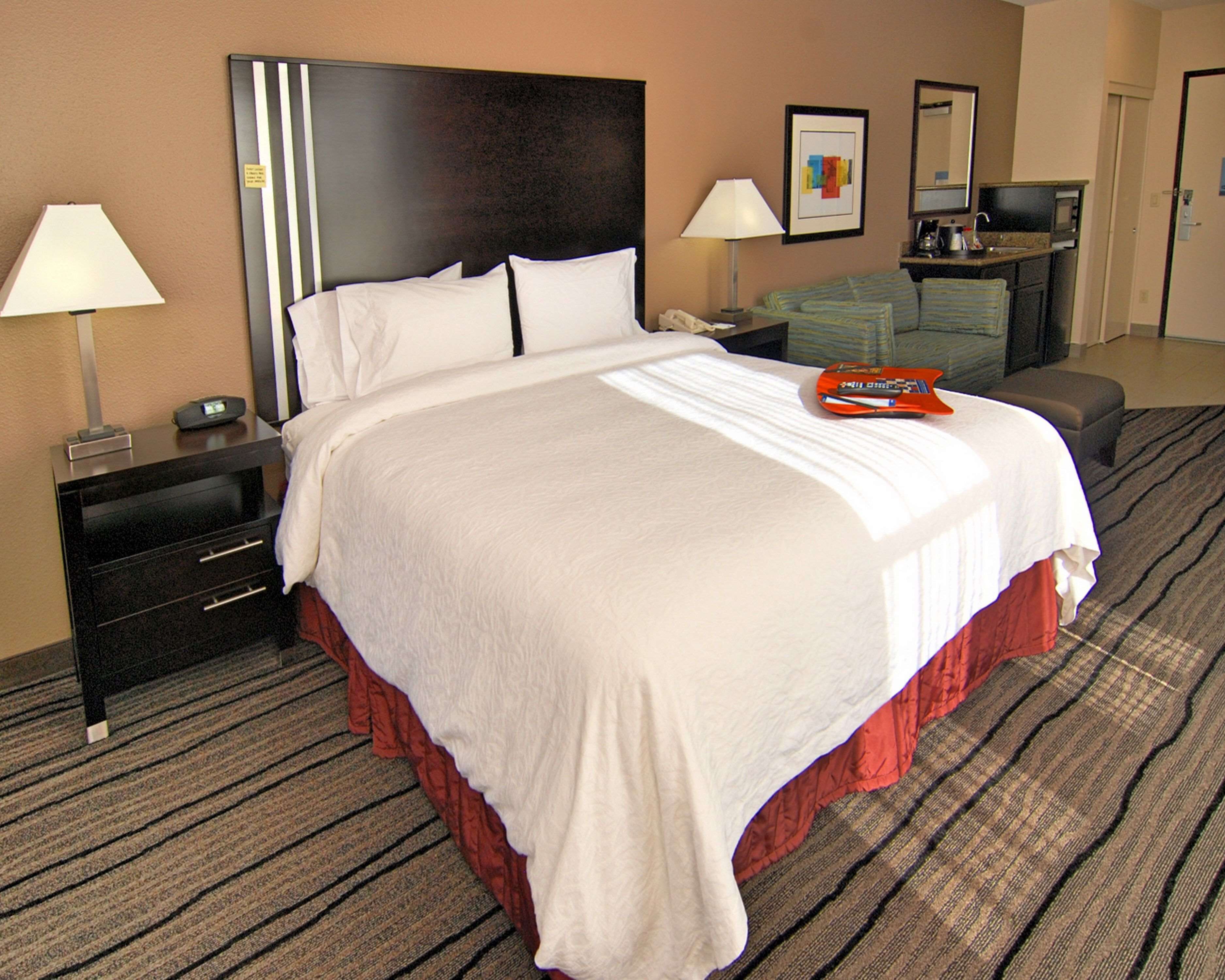 Quarto de hotel com uma cama grande, duas mesinhas de cabeceira, uma escrivaninha com cadeira, micro-ondas e cafeteira.