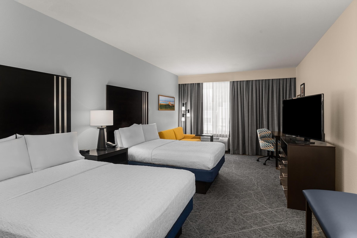 A hotel room with two beds, a desk, a chair, a television, and a window with curtains.