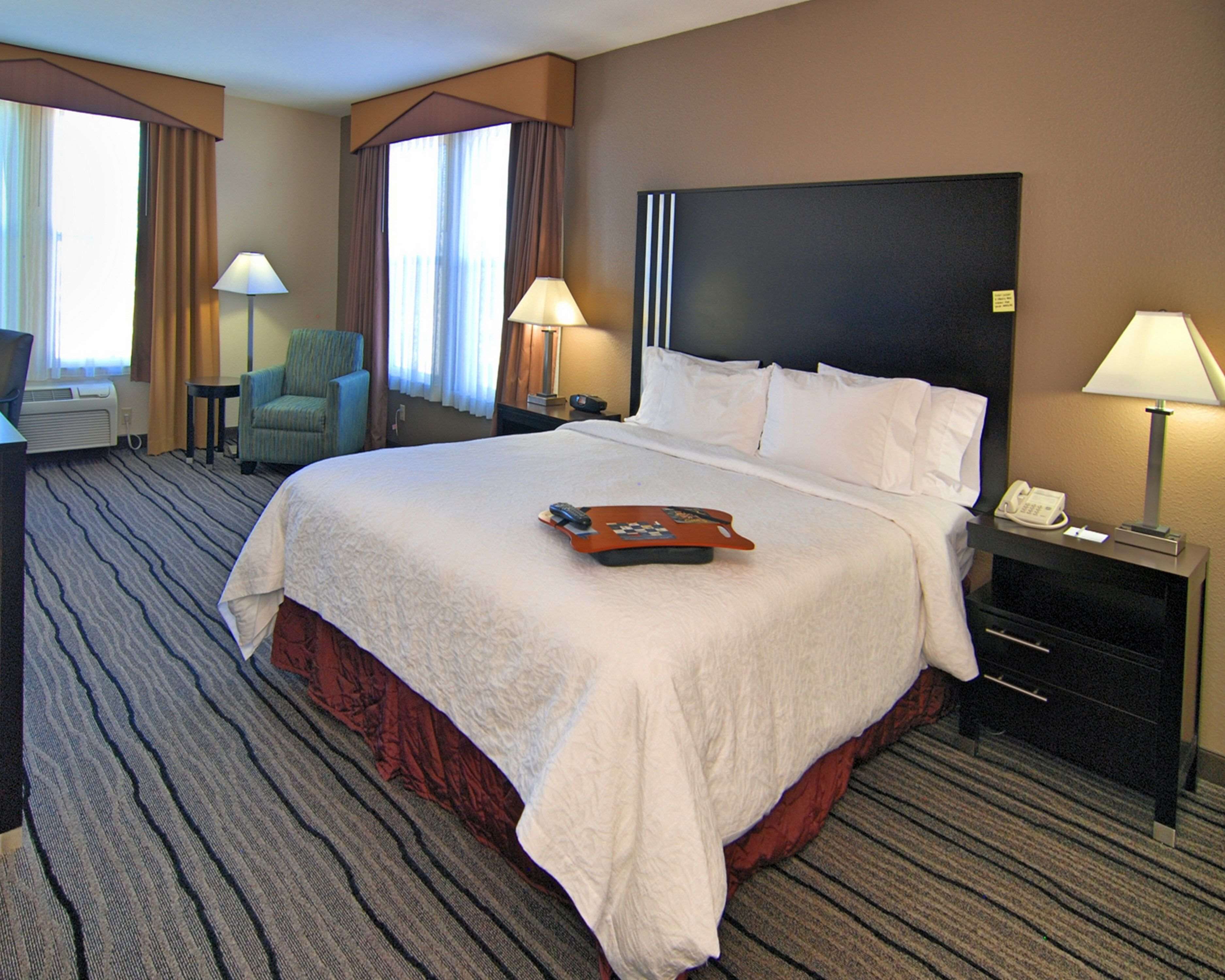 A hotel room with a large bed, a desk with a telephone, a chair, and a lamp.