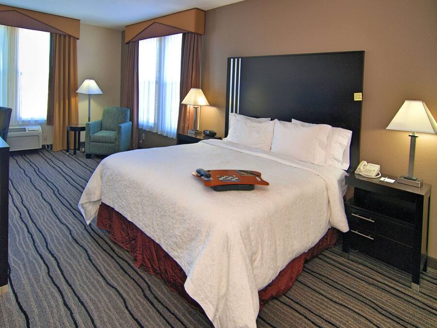 A hotel room with a large bed, a desk with a telephone, a chair, and a lamp.