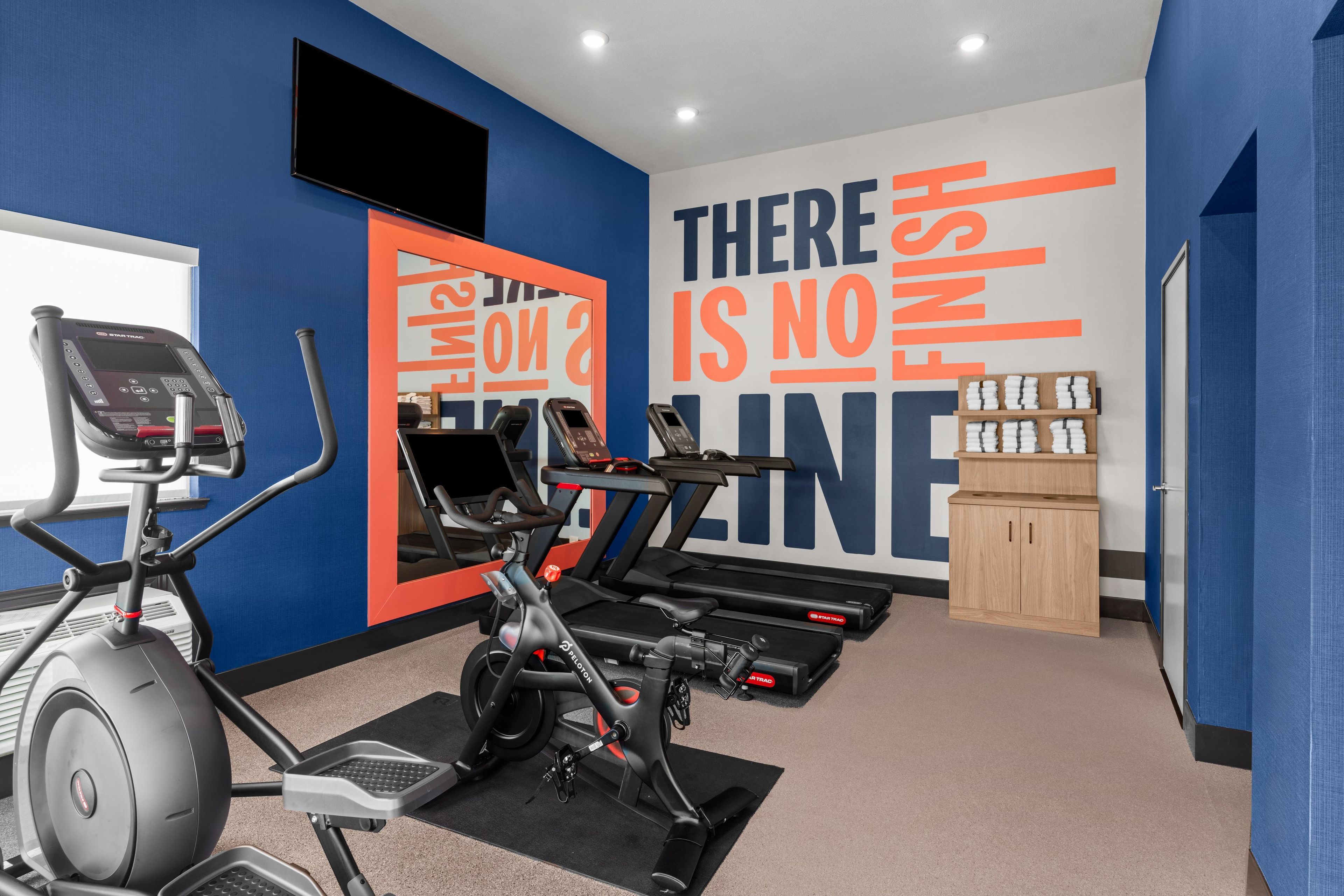 Une salle de sport équipée de matériel d’exercice, dotée d’un mur d’inspiration et d’un meuble de rangement.