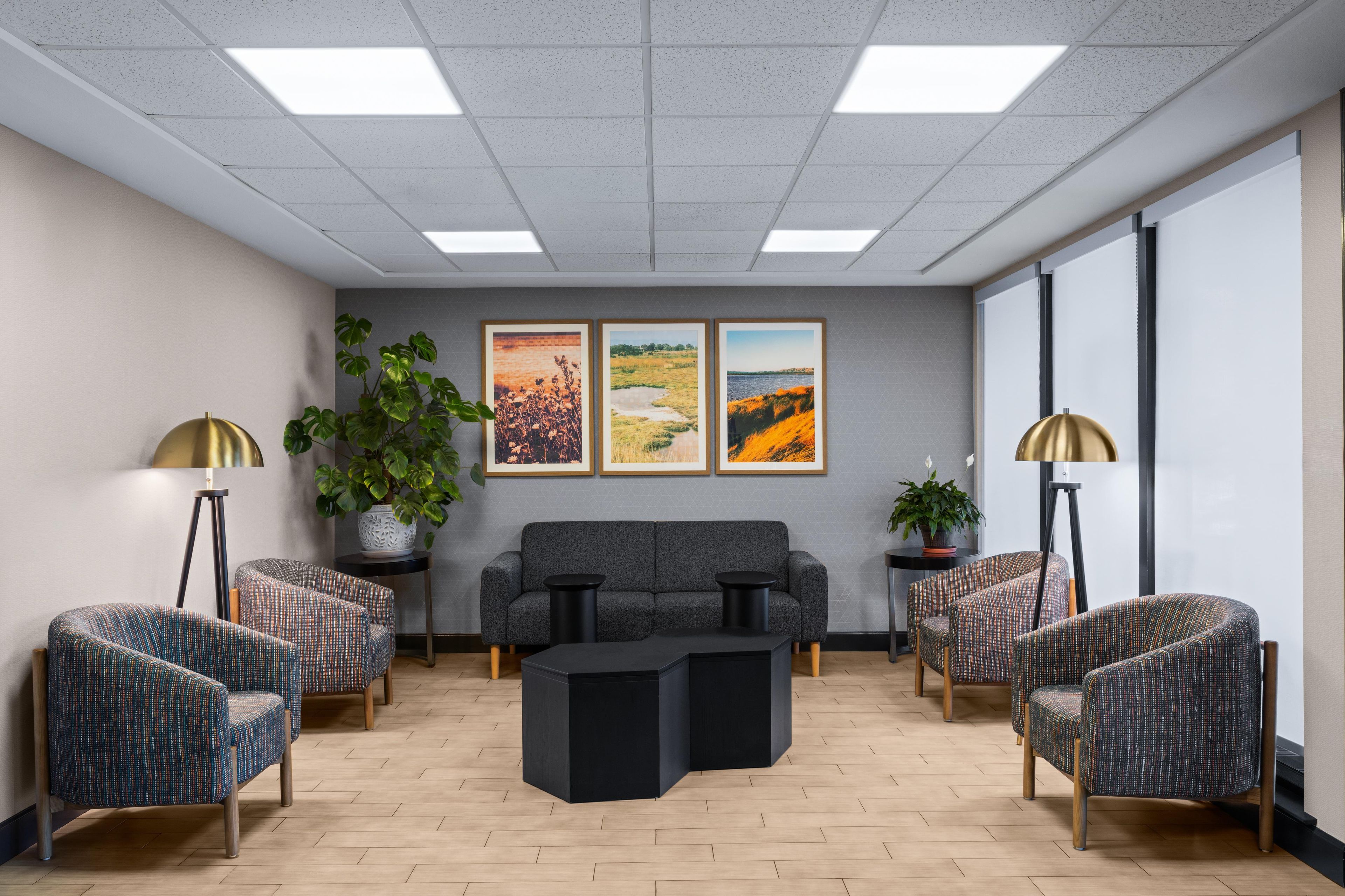 Un espace d’attente moderne, aménagé avec un canapé, des fauteuils, une table basse et des œuvres d’art accrochées au mur.