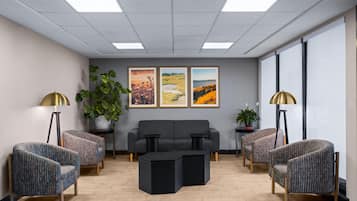 Un espace d’attente moderne, aménagé avec un canapé, des fauteuils, une table basse et des œuvres d’art accrochées au mur.
