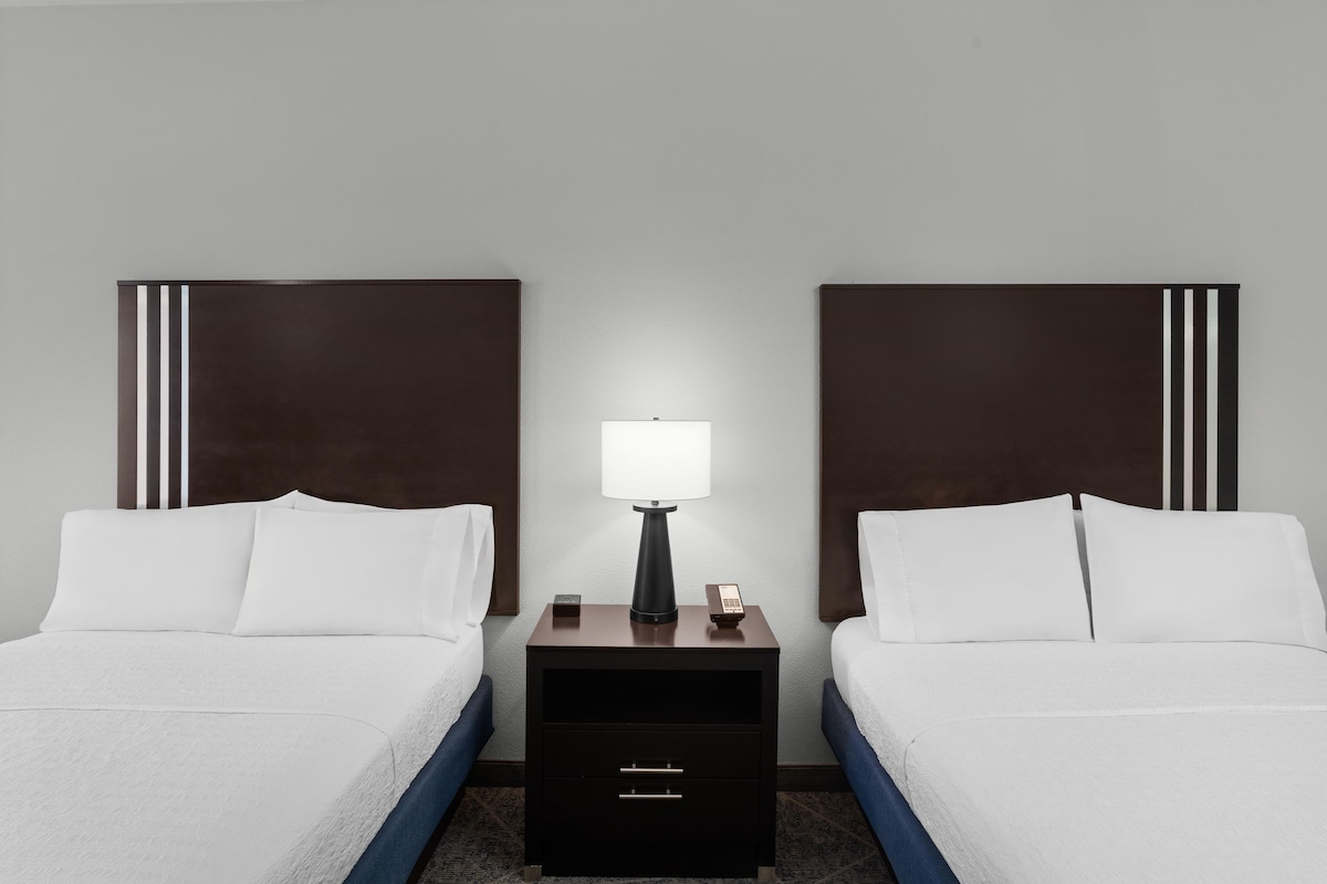 A hotel room with two beds, a nightstand with a lamp, and a drawer.
