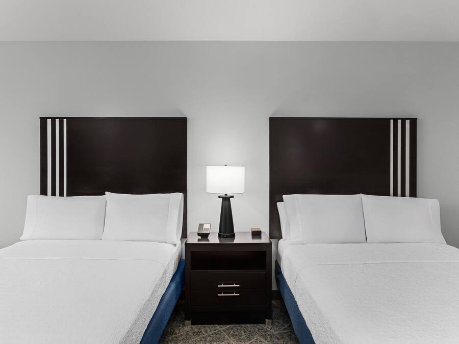 Une chambre d’hôtel avec deux lits, une table de chevet avec une lampe et une commode.