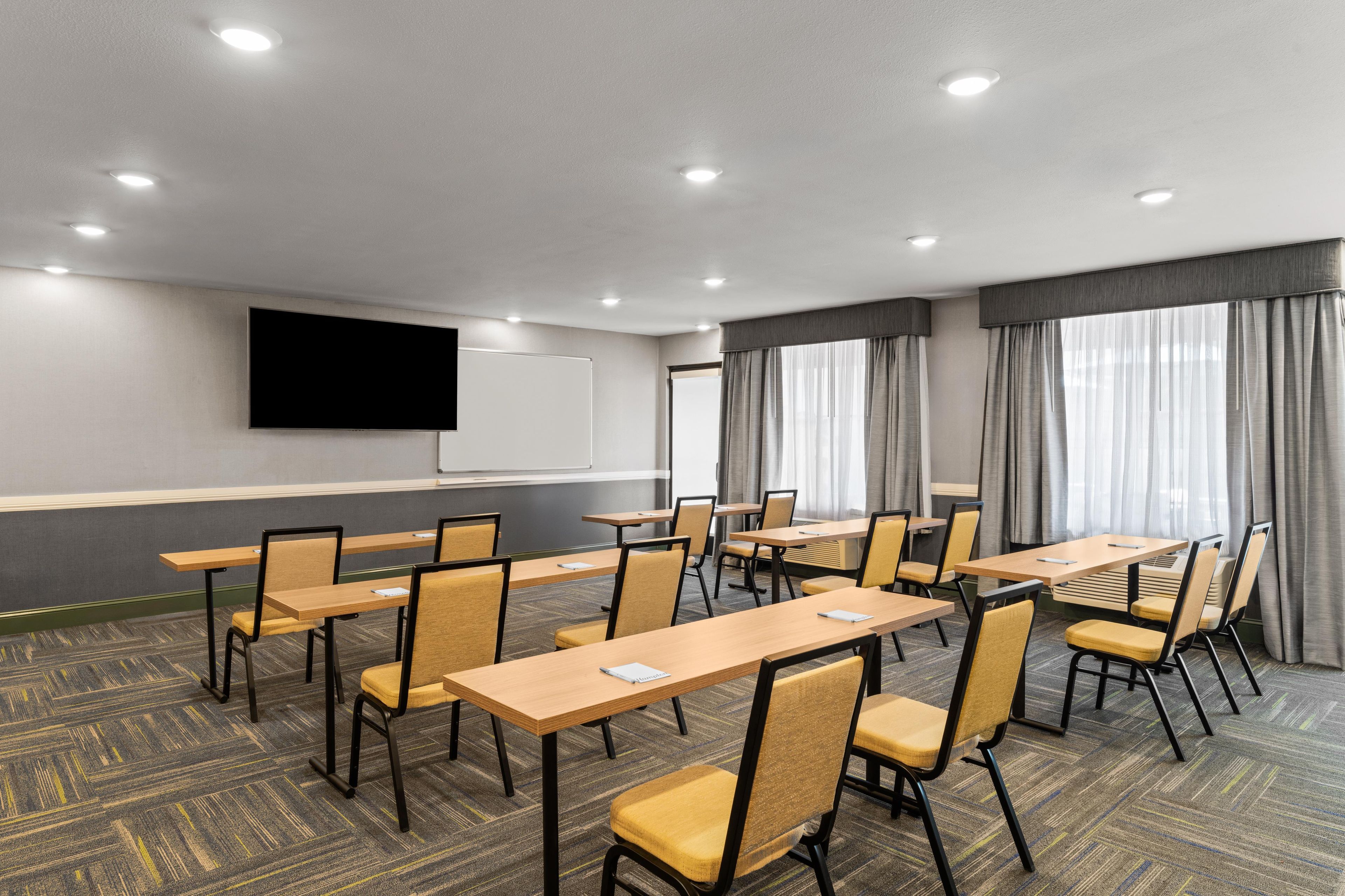 A conference room with multiple tables and chairs, a projector screen, and a large window with curtains.