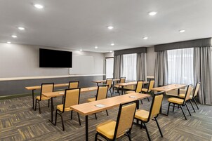 Un salón de conferencias con varias mesas y sillas, una pantalla de proyector y un amplio ventanal con cortinas.