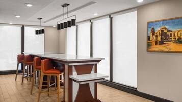 Uma área de bar moderna com bancada de mármore, banquetas de madeira e iluminação pendente.