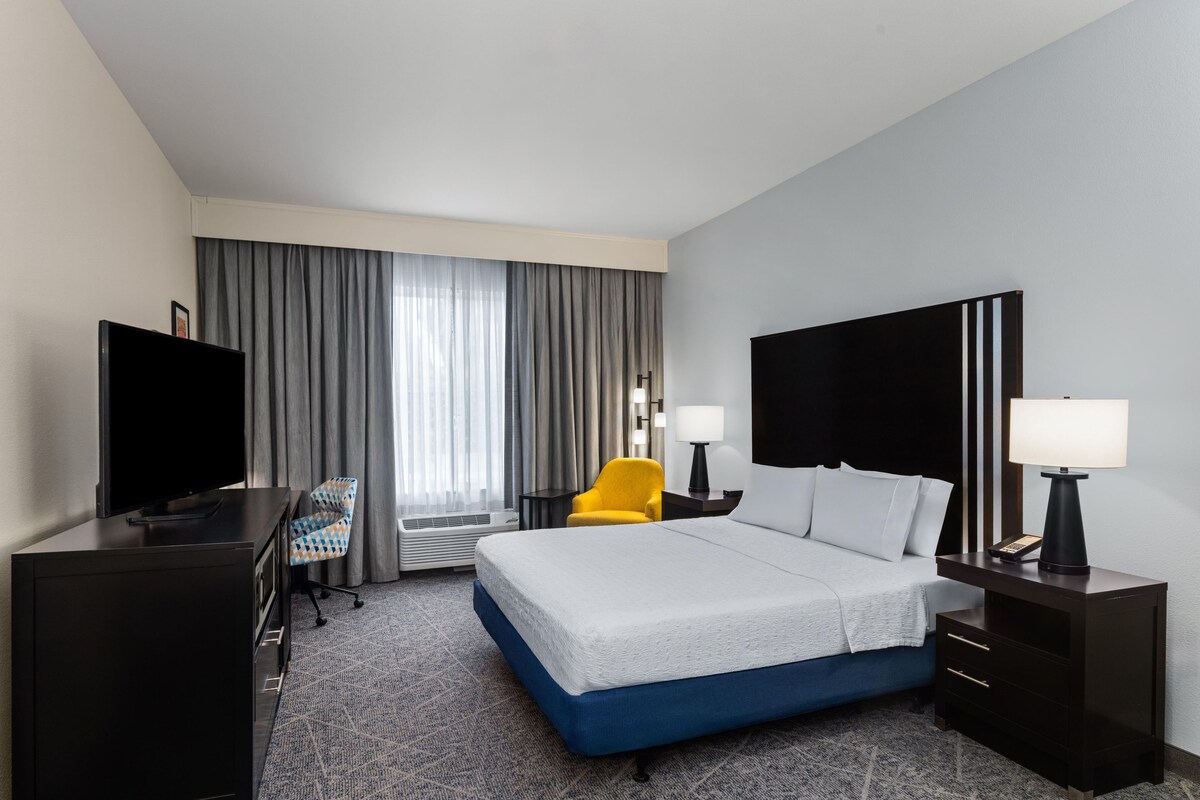 A hotel room with a bed, a desk, a television, a chair, and a window with curtains.
