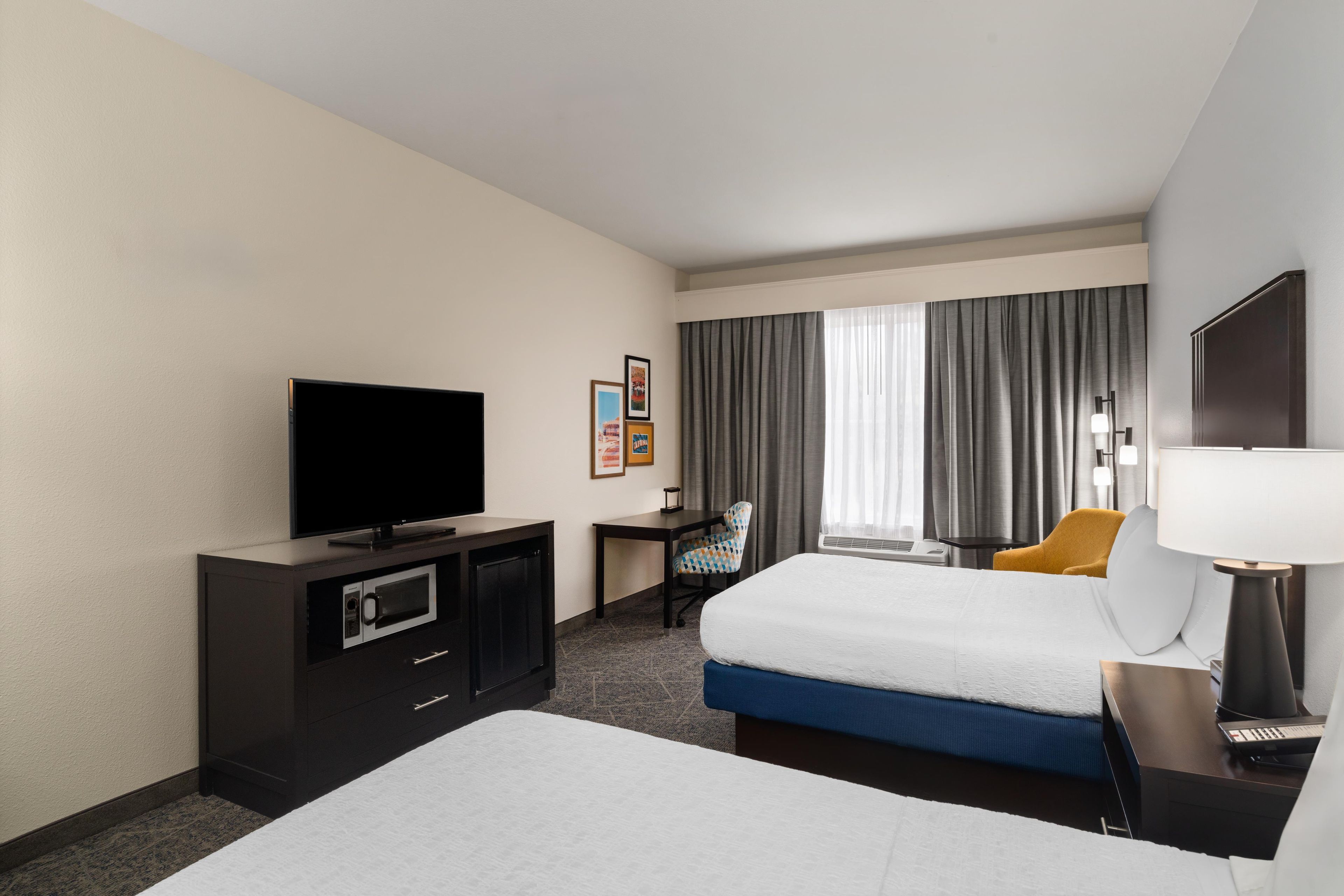 A hotel room with a bed, a desk, a television, a microwave, and a window with curtains.