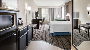 Quarto de hotel com cama, escrivaninha, cadeira, televisão e minibar.