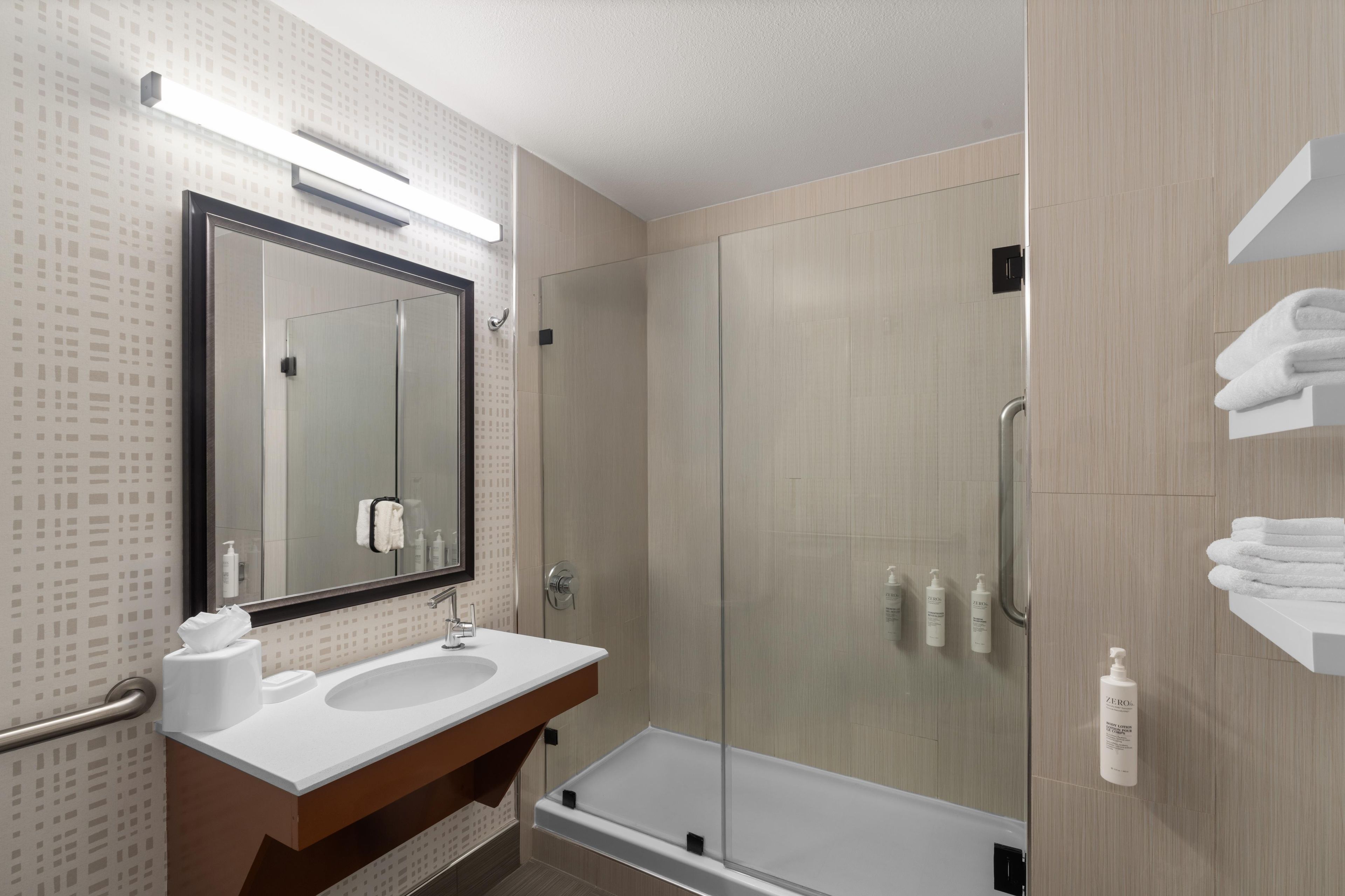 A modern bathroom with a glass-enclosed shower, a large mirror, and a white sink.