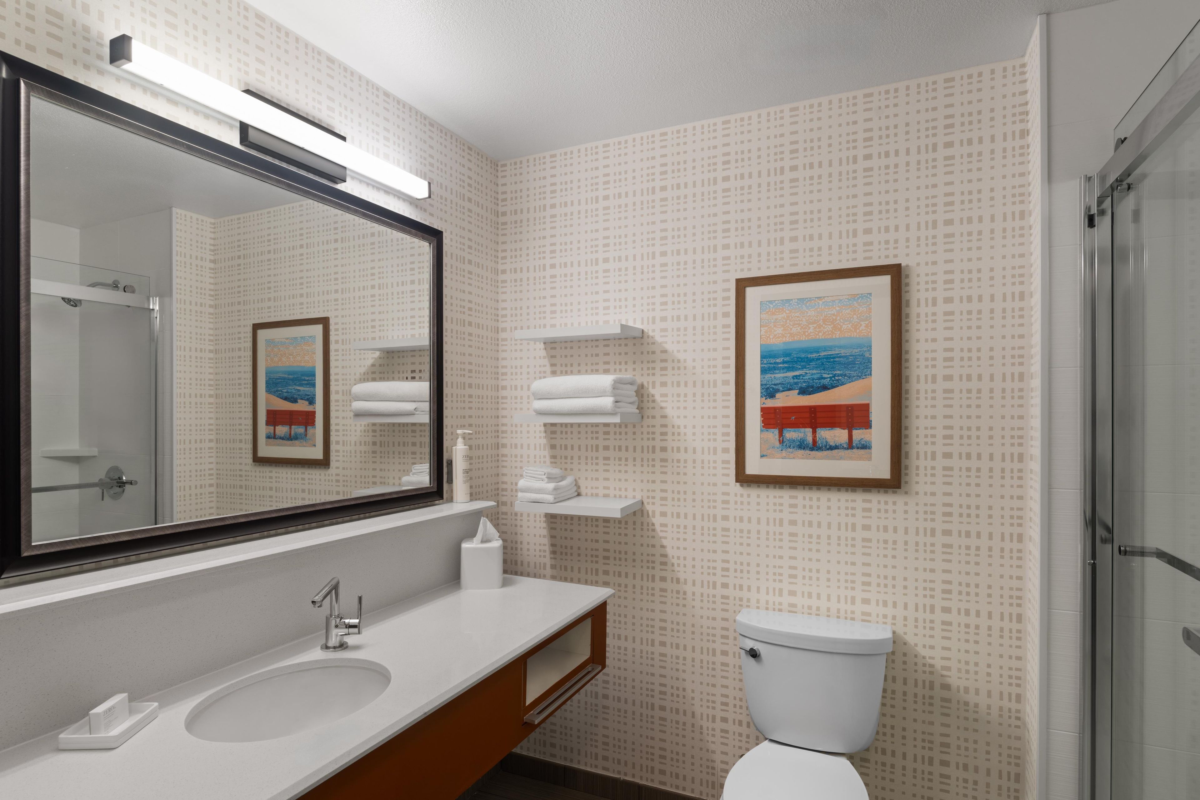 Une salle de bain avec un grand miroir, deux lavabos, des toilettes et une douche.