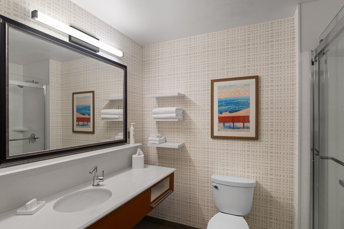 A bathroom with a large mirror, two sinks, a toilet, and a shower.