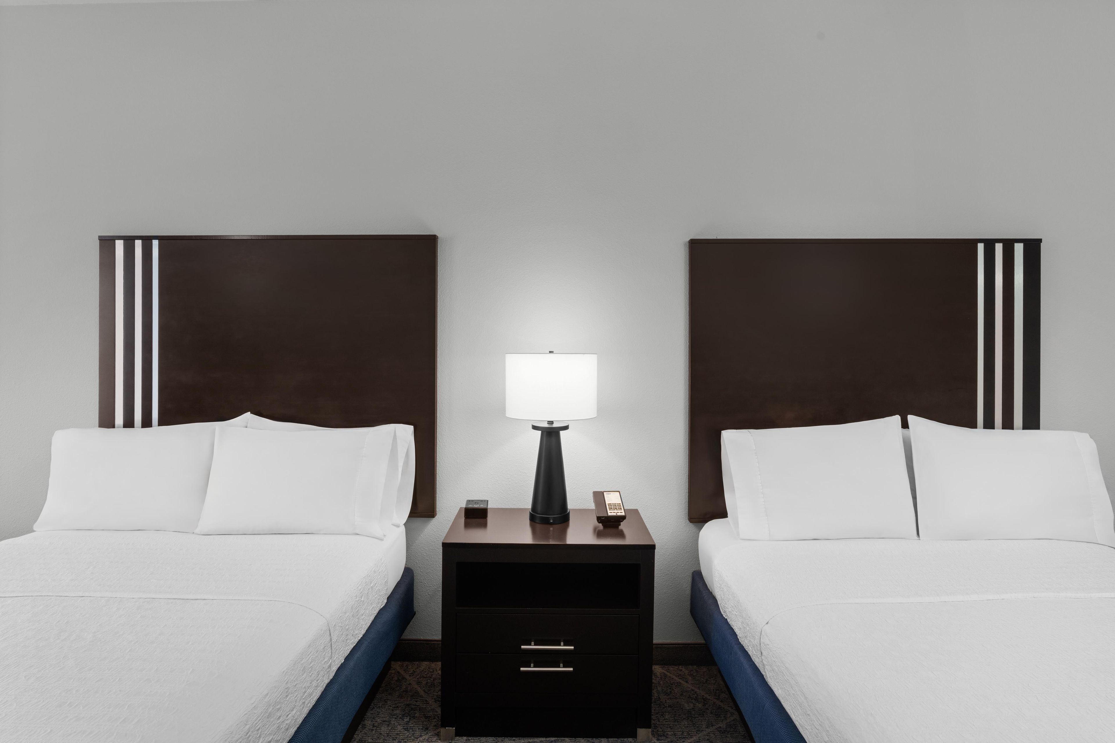 A hotel room with two beds, a nightstand with a lamp, and a drawer.