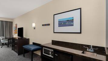 A hotel room with a desk, chair, television, microwave, and a framed picture of a marina.