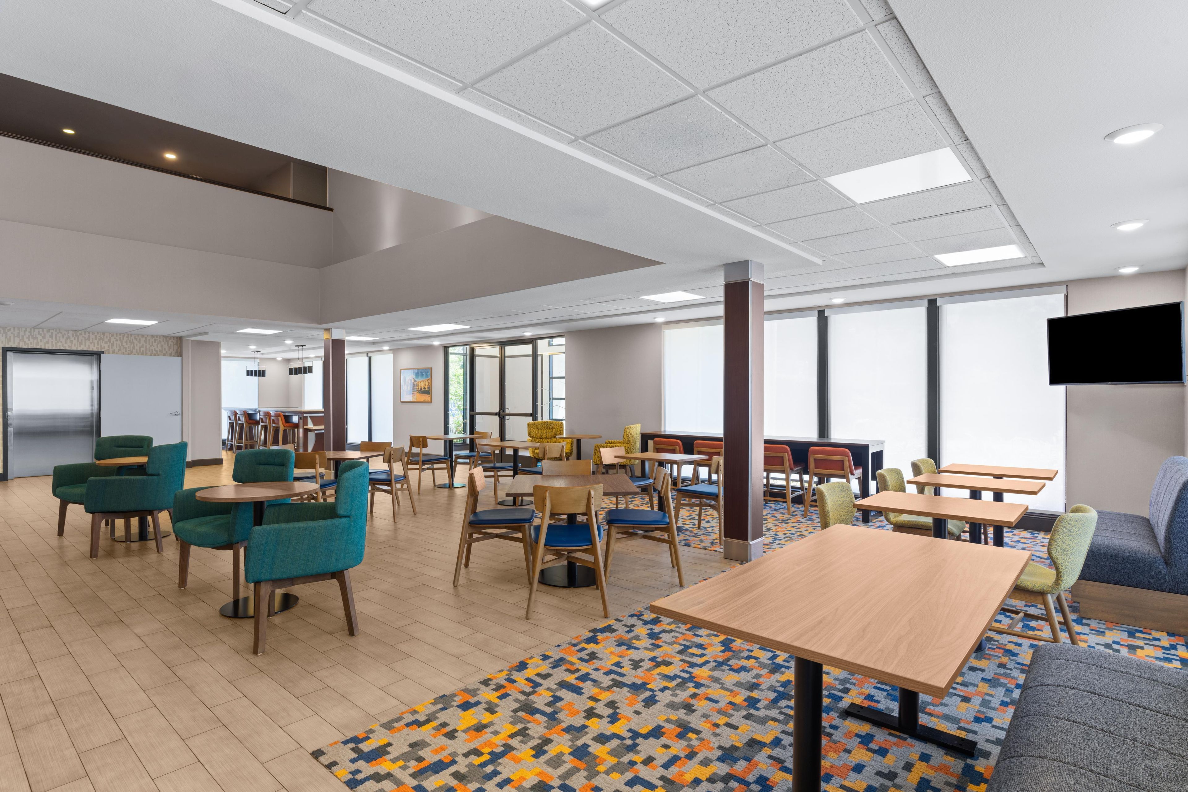 A spacious indoor area with multiple tables and chairs, large windows, and a patterned floor.